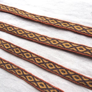 May include: Three brown and gold woven ribbon trims with a geometric diamond pattern.