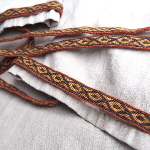 May include: Close-up of a brown and black woven trim with a diamond pattern. The trim is on a light gray fabric.
