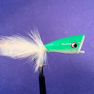 May include: A green and white fishing lure with a white feather tail. The lure has a green body with a white head and a red and black eye. The lure is designed to attract fish.