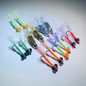 May include: A collection of colorful fishing lures. Each lure features a hook, a body with a beaded design, and a shimmering tail. The lures come in various colors, including green, silver, gold, orange, and pink.