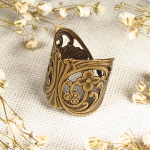 Puede incluir: Un anillo de metal dorado con un intrincado dise&ntilde;o floral. El anillo est&aacute; abierto por un lado y tiene un delicado patr&oacute;n de filigrana.