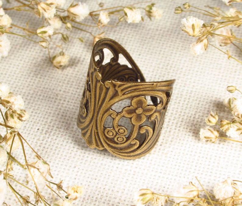 Puede incluir: Un anillo de metal dorado con un intrincado dise&ntilde;o floral. El anillo est&aacute; abierto por un lado y tiene un delicado patr&oacute;n de filigrana.