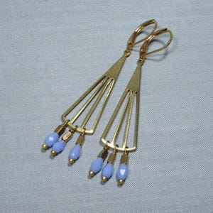 May include: A pair of gold tone earrings with a geometric design and light blue glass beads hanging from the bottom.