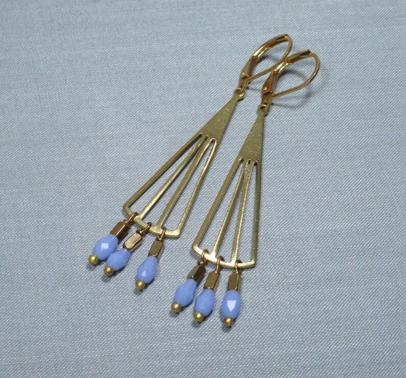 May include: A pair of gold tone earrings with a geometric design and light blue glass beads hanging from the bottom.