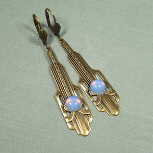 May include: A pair of gold-tone earrings with a geometric design and a light blue opal stone in the center of each earring.