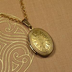 Könnte beinhalten: Eine goldfarbene Halskette mit einem detaillierten Blumenmuster. Das Medaillon ist oval und hat eine Scharnieröffnung.