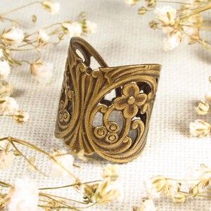 Puede incluir: Un anillo de metal dorado con un delicado dise&ntilde;o floral. El anillo es abierto y ajustable, lo que lo convierte en un accesorio vers&aacute;til.