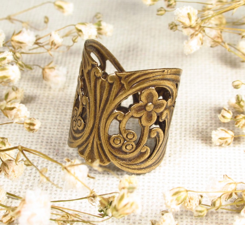 Puede incluir: Un anillo de metal dorado con un delicado dise&ntilde;o floral. El anillo es abierto y ajustable, lo que lo convierte en un accesorio vers&aacute;til.