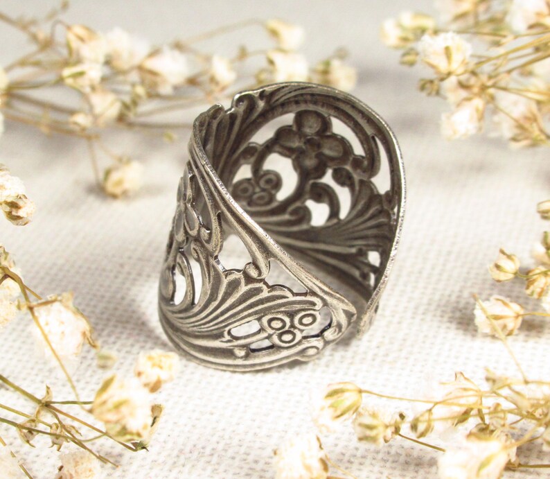 May include: A silver filigree ring with a delicate floral design. The ring is open and adjustable to fit different finger sizes.