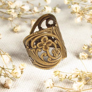 Puede incluir: Un anillo de metal dorado con un delicado dise&ntilde;o floral. El anillo es ancho y tiene un patr&oacute;n de corte.