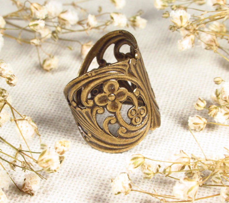 Puede incluir: Un anillo de metal dorado con un delicado dise&ntilde;o floral. El anillo es ancho y tiene un patr&oacute;n de corte.