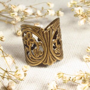 Puede incluir: Un anillo de metal dorado con un dise&ntilde;o floral decorativo. El anillo es ancho y tiene un patr&oacute;n de filigrana.