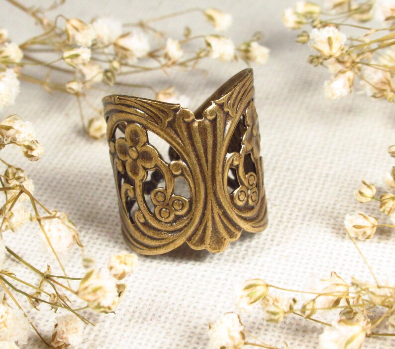 Puede incluir: Un anillo de metal dorado con un dise&ntilde;o floral decorativo. El anillo es ancho y tiene un patr&oacute;n de filigrana.