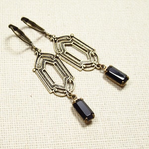 Peut inclure: Une paire de boucles d'oreilles dorées avec un motif géométrique et des accents de pierres précieuses noires.