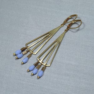 May include: A pair of gold earrings with a geometric design and blue glass beads hanging from the bottom.