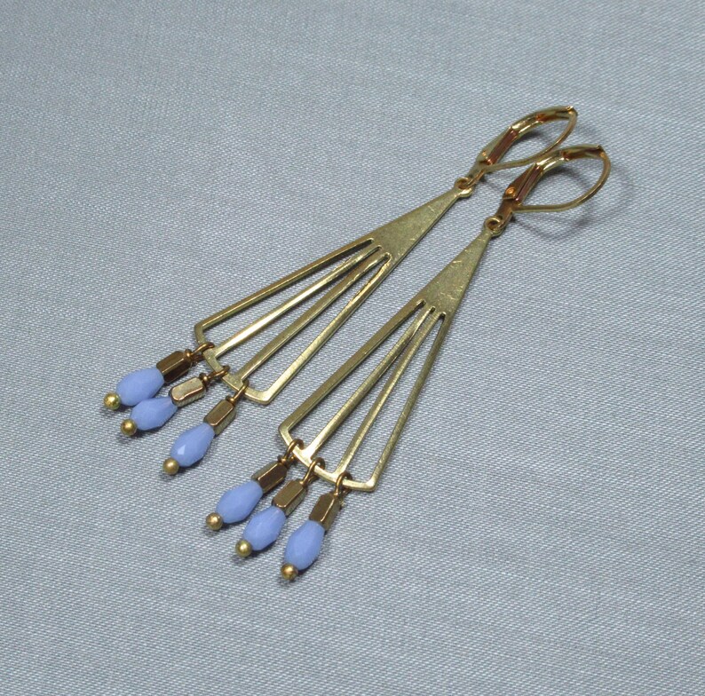 May include: A pair of gold earrings with a geometric design and blue glass beads hanging from the bottom.