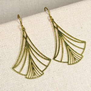 May include: A pair of gold-toned earrings with a delicate, fan-shaped design. The earrings are made of metal and have a simple, elegant style.