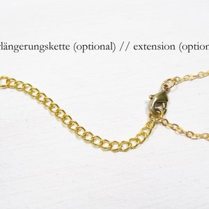 May include: Gold-colored necklace chain extension with a lobster clasp and a small chain. The extension is designed to add length to necklaces. The text "extension (optional)" is visible.