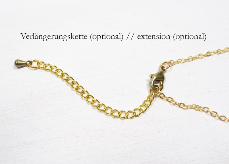 May include: Gold-colored necklace chain extension with a lobster clasp and a small chain. The extension is designed to add length to necklaces. The text "extension (optional)" is visible.