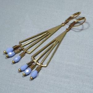May include: A pair of gold earrings with a geometric design and light blue glass beads hanging from the bottom.