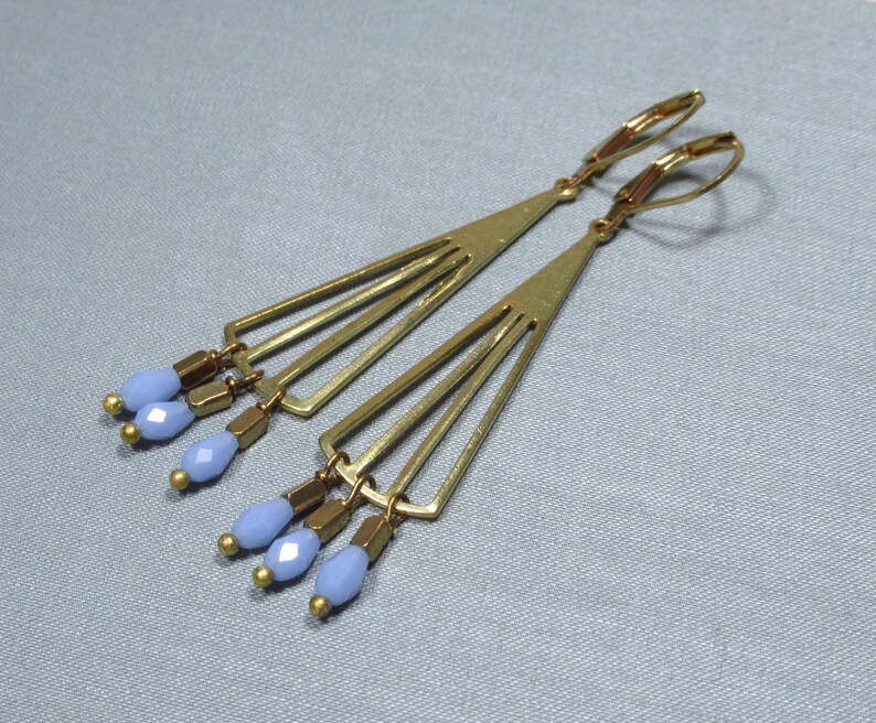 May include: A pair of gold earrings with a geometric design and light blue glass beads hanging from the bottom.
