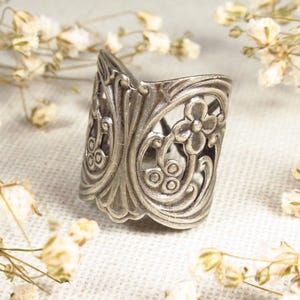 May include: A silver ring with a floral design. The ring is made of metal and has a delicate, intricate pattern.