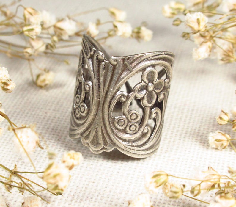 May include: A silver ring with a floral design. The ring is made of metal and has a delicate, intricate pattern.