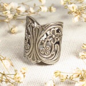 May include: A silver ring with a floral design. The ring is made of metal and has a delicate, intricate pattern.