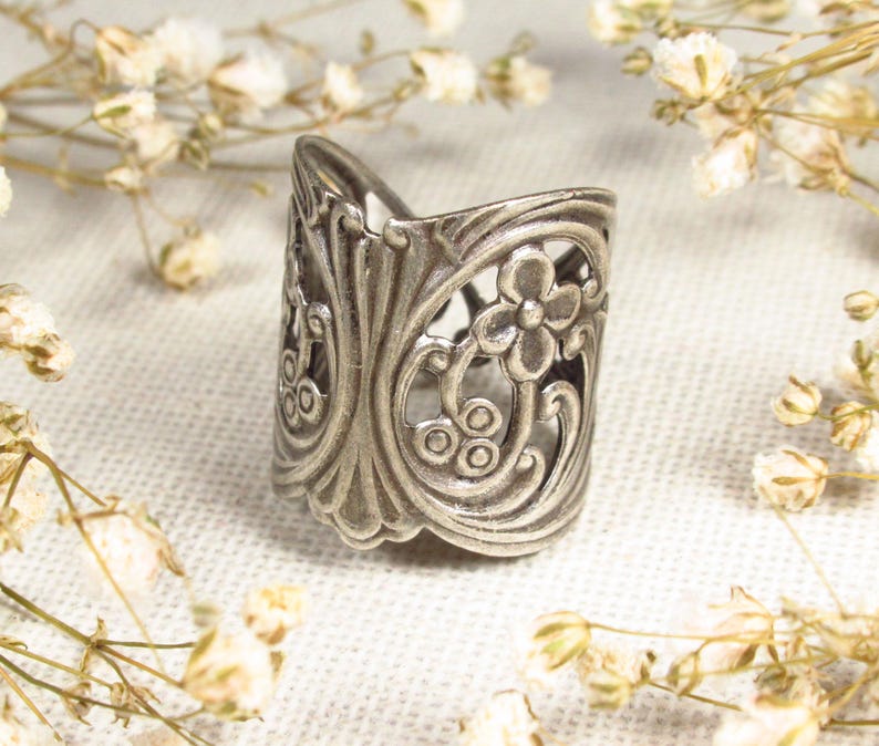 May include: A silver ring with a floral design. The ring is made of metal and has a delicate, intricate pattern.