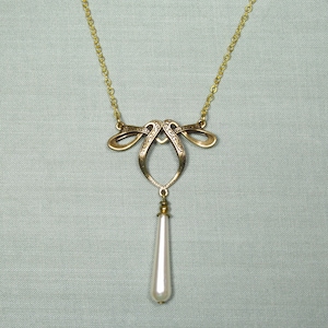 May include: A gold necklace with a delicate, ornate pendant featuring a teardrop-shaped pearl.