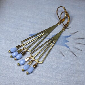 May include: A pair of gold tone earrings with a geometric design and light blue glass beads.
