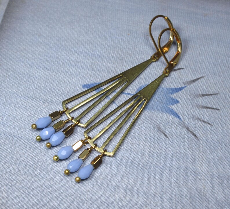 May include: A pair of gold tone earrings with a geometric design and light blue glass beads.