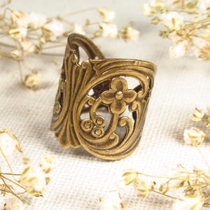 Puede incluir: Un anillo de metal dorado con un dise&ntilde;o floral decorativo. El anillo est&aacute; abierto y tiene una banda ancha.