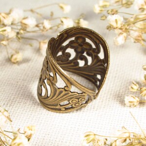 Puede incluir: Un anillo de metal dorado con un dise&ntilde;o delicado e intrincado. El anillo est&aacute; abierto y tiene una banda ancha.