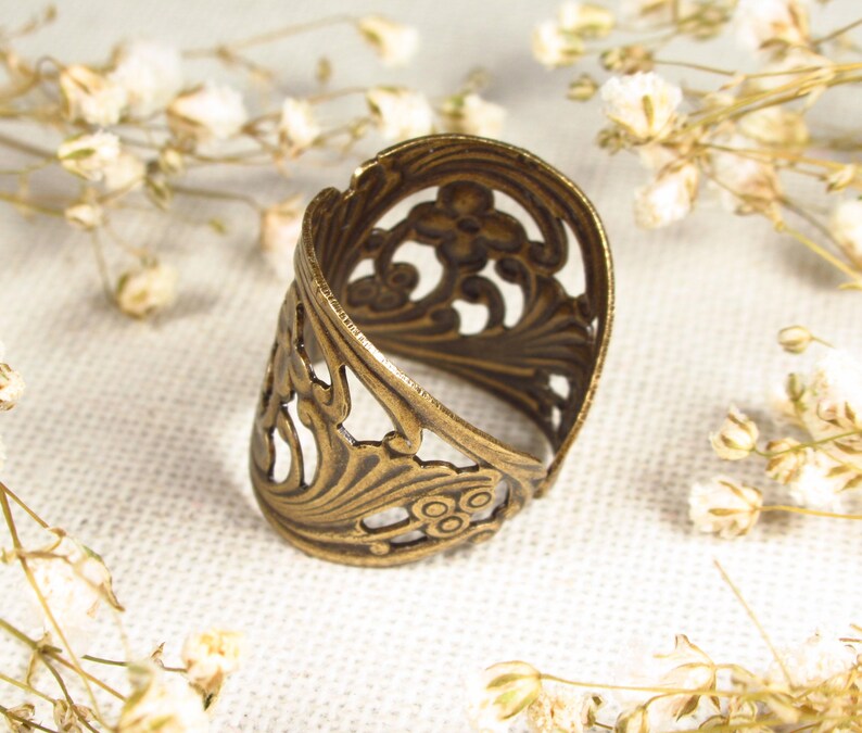 Puede incluir: Un anillo de metal dorado con un dise&ntilde;o delicado e intrincado. El anillo est&aacute; abierto y tiene una banda ancha.