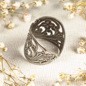 May include: A silver filigree ring with a delicate floral design. The ring is open and has a wide band.