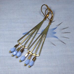 May include: Gold geometric earrings with a fan-shaped design and light blue glass beads dangling from the bottom.