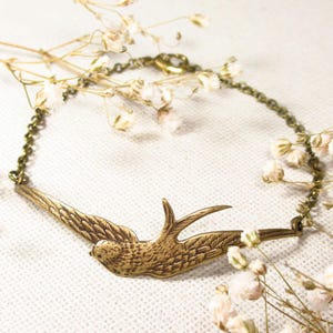 May include: A gold-toned bracelet featuring a delicate chain and a detailed bird charm. The bird is in flight with its wings outstretched.