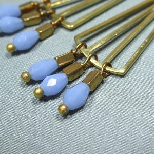 May include: Gold geometric earrings with light blue glass beads dangling from the bottom.