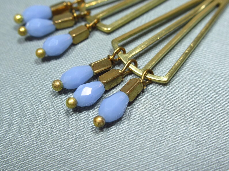 May include: Gold geometric earrings with light blue glass beads dangling from the bottom.