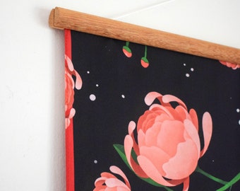 May include: A black canvas print with a floral design featuring pink flowers and green leaves. The print is mounted on a wooden frame with a string for hanging.