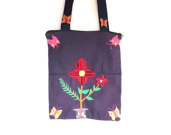 May include: A dark purple tote bag with embroidered floral and butterfly designs. The bag features a large red flower with a yellow center, green leaves, and smaller red flowers. Pink, yellow, and orange butterflies are embroidered on the bag.