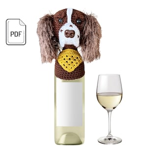 May include: A bottle of white wine with a decorative, handmade crochet dog head bottle stopper. The dog stopper is brown and white with a yellow collar. A wine glass with white wine is next to the bottle. The image also includes a PDF icon.