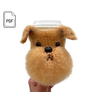 May include: A brown and white plush dog head cup cozy. The cozy is made to fit a standard size cup.