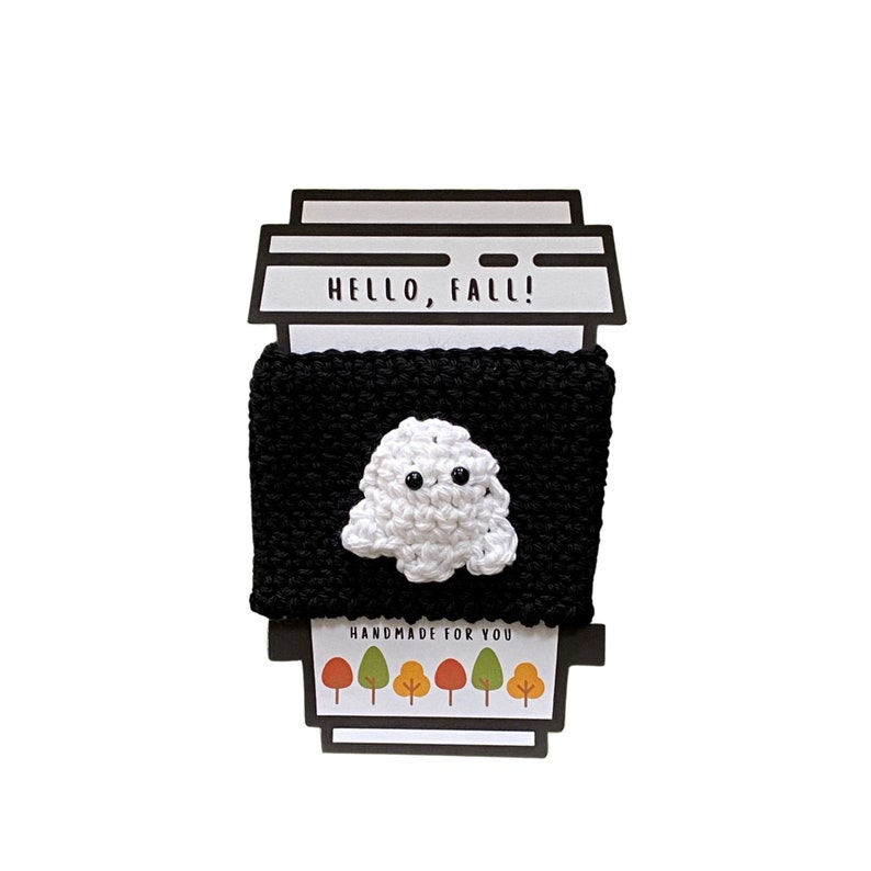 May include: Black and white crocheted coffee cup cozy with a ghost design. The cozy has the text "Hello, Fall!" and "Handmade for you" printed on it.