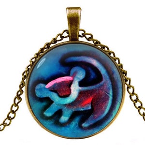 May include: A bronze chain necklace with a round glass pendant featuring a blue, pink, and purple lion king symbol.