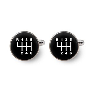 Pode incluir: Um par de abotoaduras redondas em tom prateado com uma face circular preta e um padrão de mudança de marchas manual em branco. O gráfico exibe as letras R, 1, 3, 5 na linha superior e 2, 4, 6 na linha inferior do diagrama de marchas.