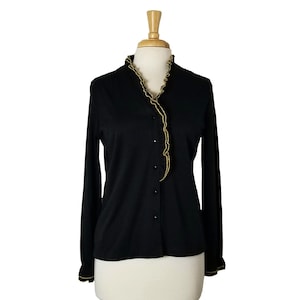 Op de afbeelding: Zwart button-down shirt met lange mouwen en gouden afwerking op de kraag, manchetten en knooplijn. Het shirt wordt op een mannequin getoond. De afwerking heeft een gerimpeld ontwerp. Het shirt heeft een klassieke, elegante stijl.