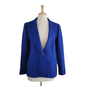 Puede incluir: Un blazer azul vibrante exhibido en un maniquí. El blazer presenta una solapa con muescas clásica, dos bolsillos delanteros y un cierre de un solo botón. La prenda está hecha de una tela suave y tiene un ajuste a medida, adecuado para uso profesional o informal.