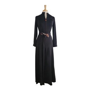 K&ouml;nnte beinhalten: Schwarzer Jumpsuit mit langen &Auml;rmeln und hohem Kragen, auf einer Schaufensterpuppe pr&auml;sentiert. Der Jumpsuit hat einen durchgehenden Rei&szlig;verschluss mit orangefarbenem Besatz und einen gemusterten G&uuml;rtel. Der weite Bein-Schnitt deutet auf einen Vintage-Stil hin.